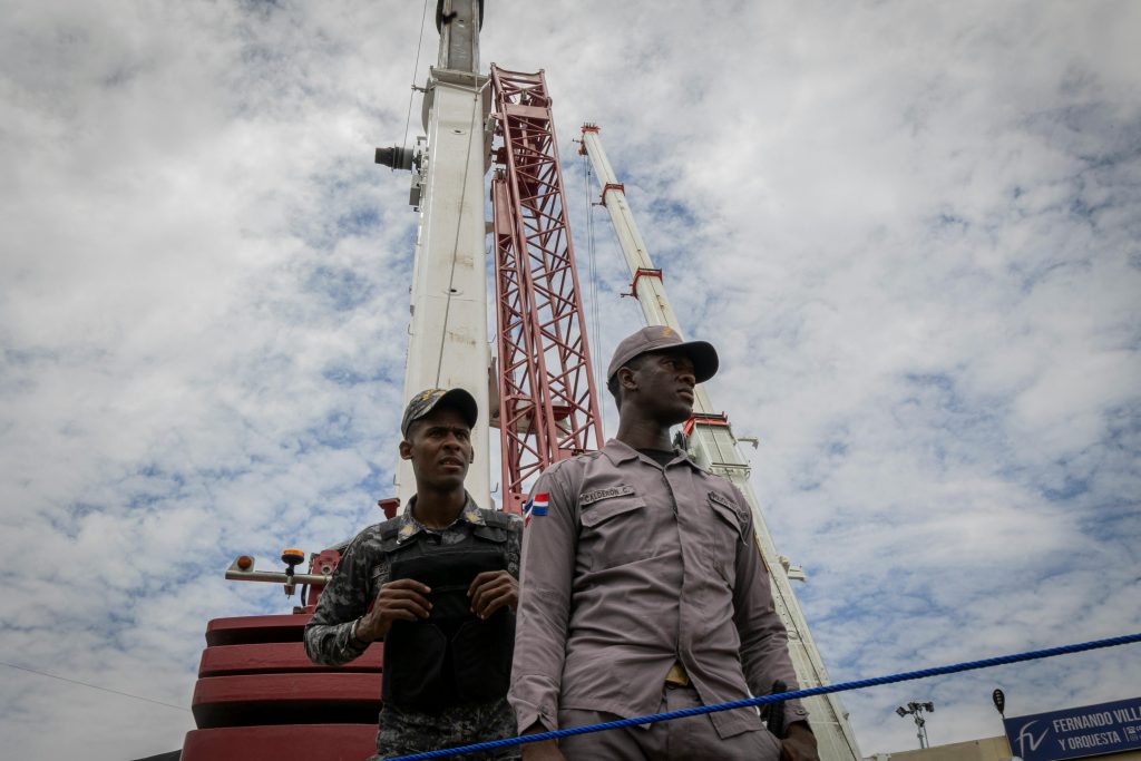 Two uniformed security officers guarding a large industrial crane under a cloudy sky.