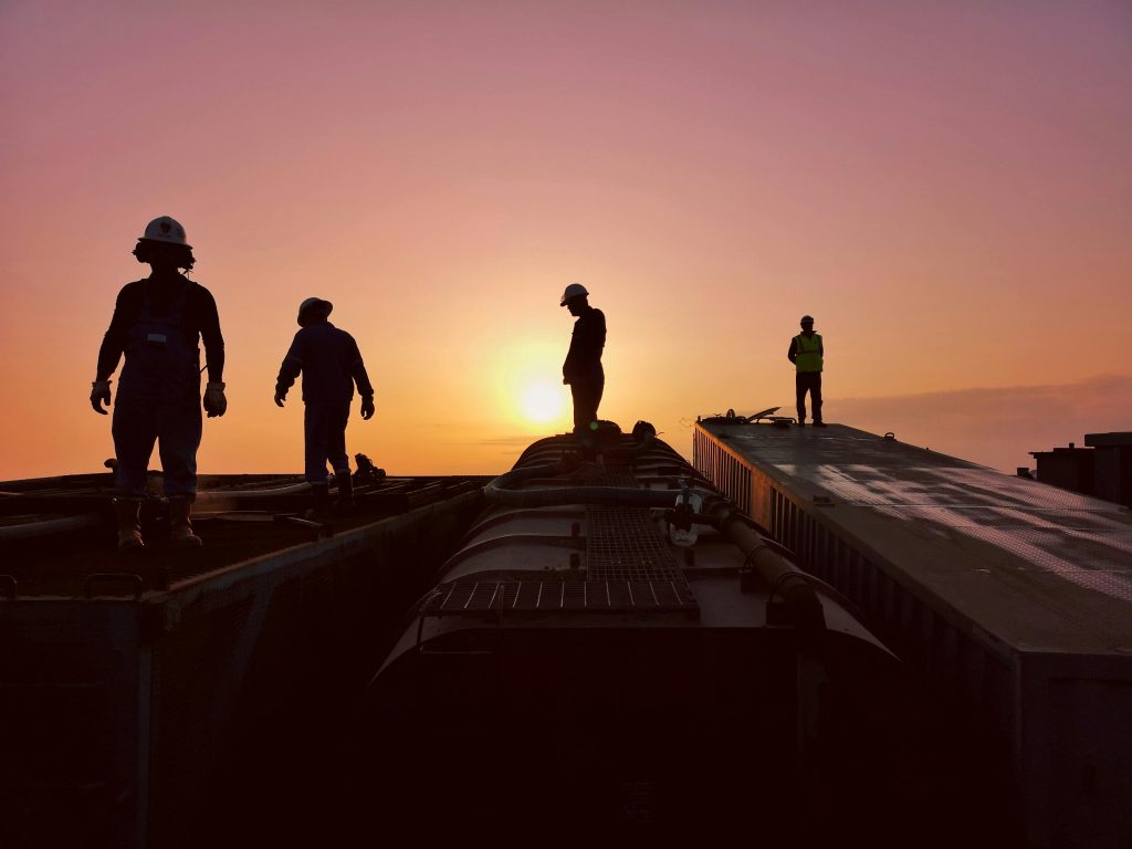Silhouettes of workers atop industrial structures against a stunning sunset backdrop.